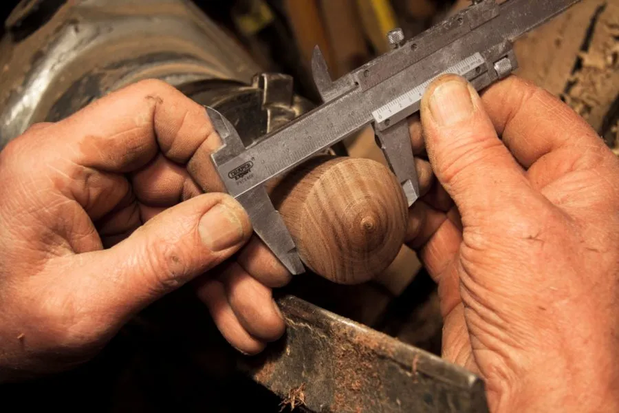 Le mani di un falegname misurano un pezzo di legno con il calibro